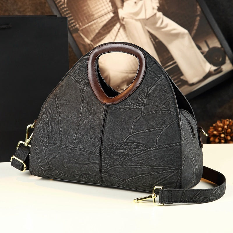 Black textured handbag with brown interior on a white surface, blurred background