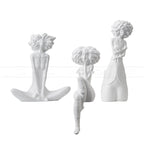 Three white ceramic wall hooks shaped like women with different hairstyles on a white background