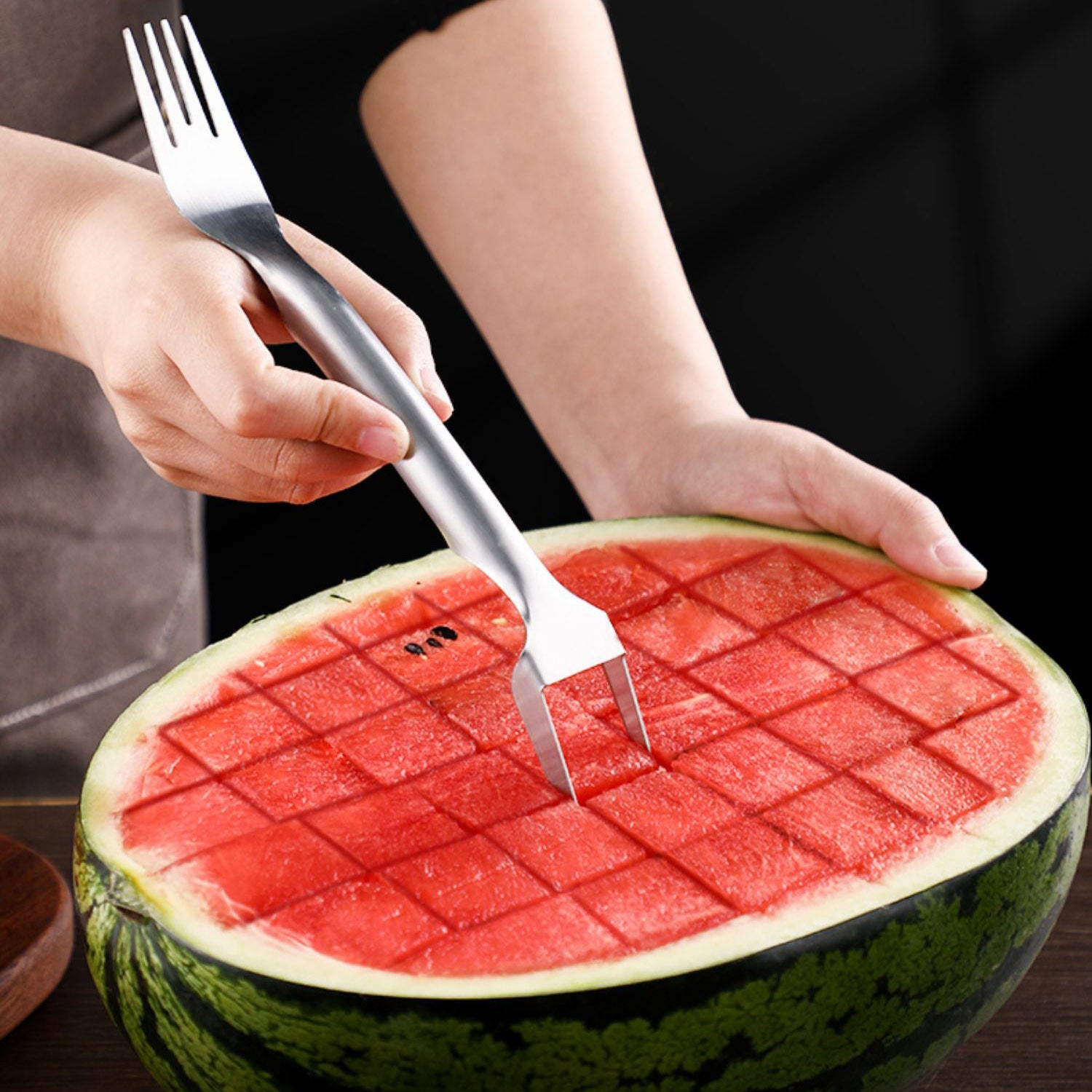 Person cutting a watermelon with a grid pattern using a fork.
