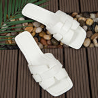 Pair of white sandals on a wooden deck with pebbles and leaves.