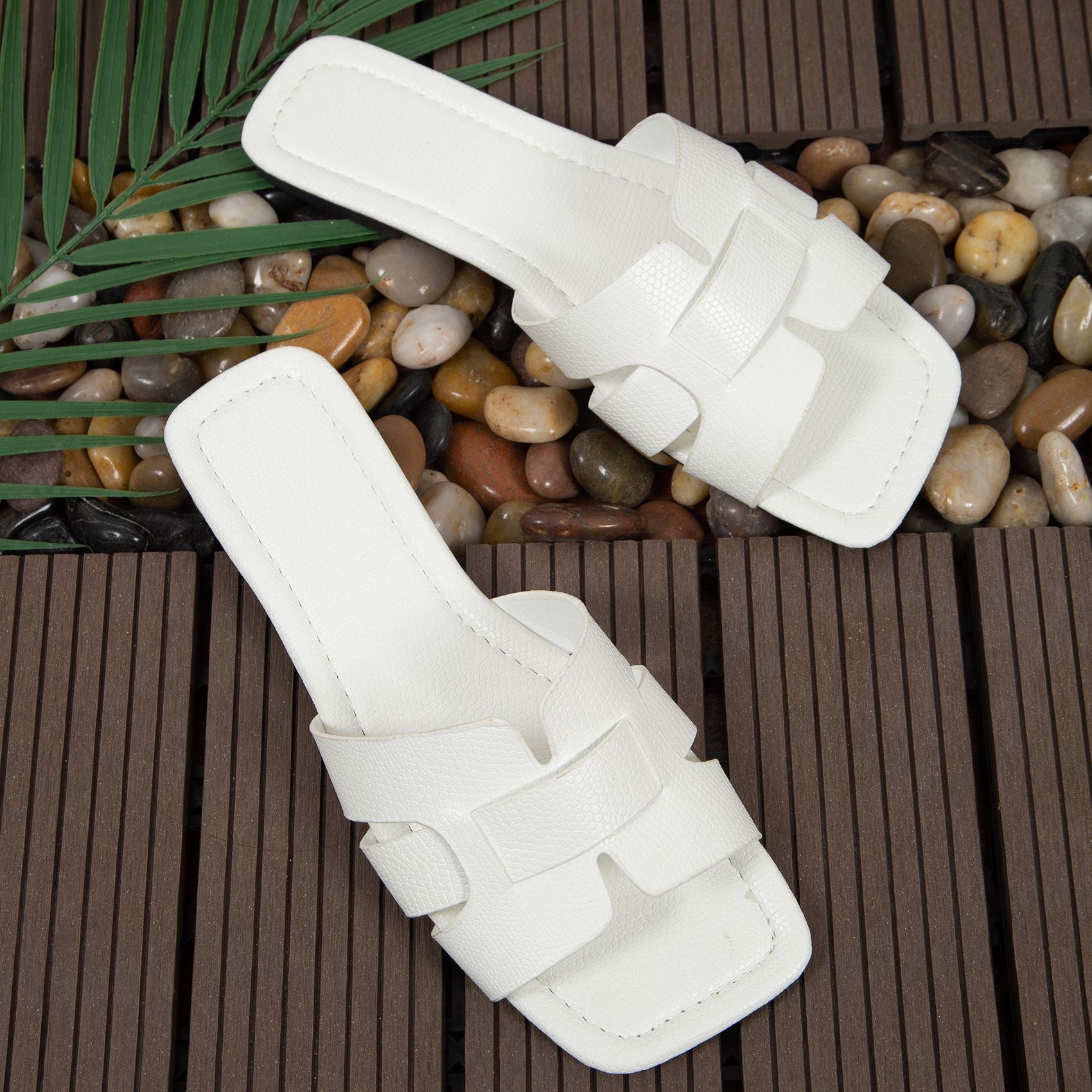Pair of white sandals on a wooden deck with pebbles and leaves.