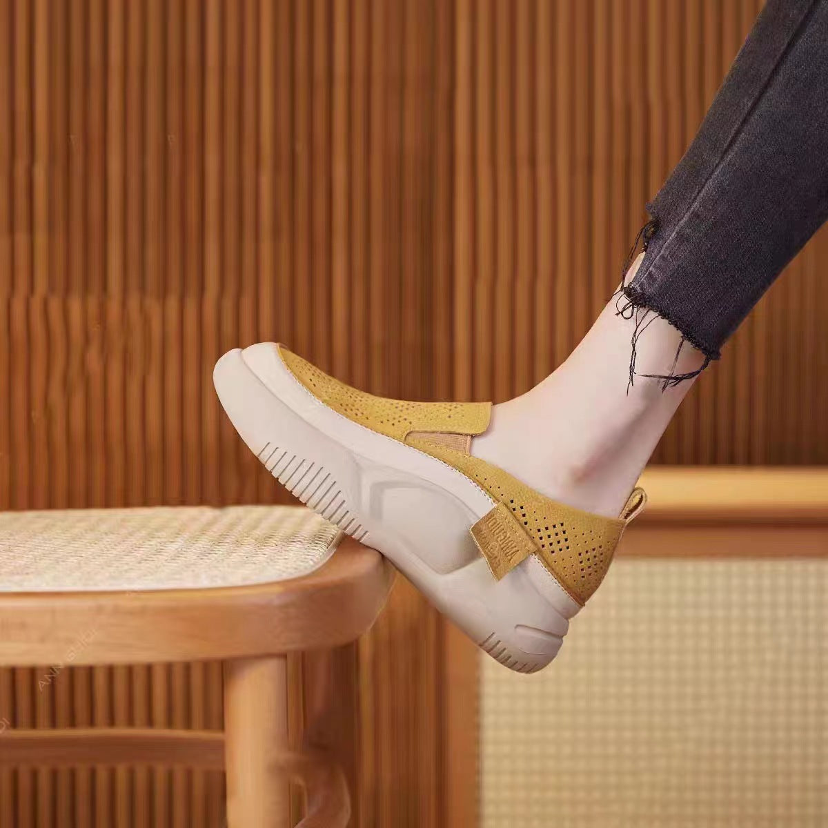 Yellow slip-on shoes with white soles worn by a person sitting on a wooden stool.