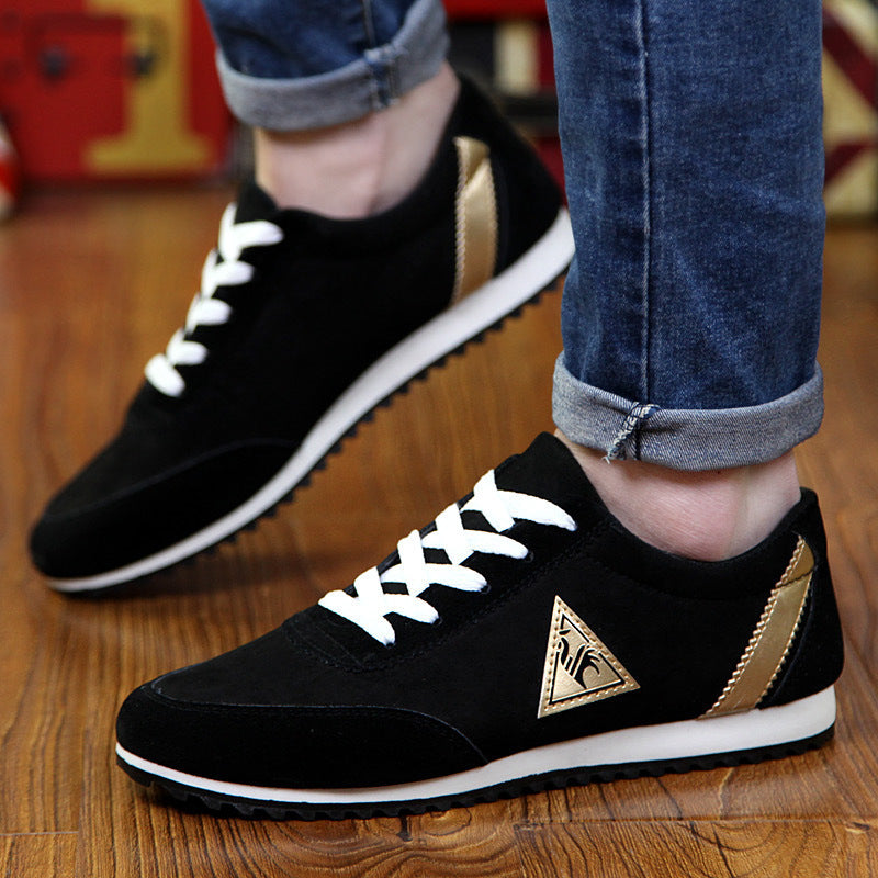 Black sneakers with white laces and a gold logo worn by a person on a wooden floor.