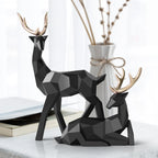 Two black geometric deer figurines on a surface with a vase and branches in the background.