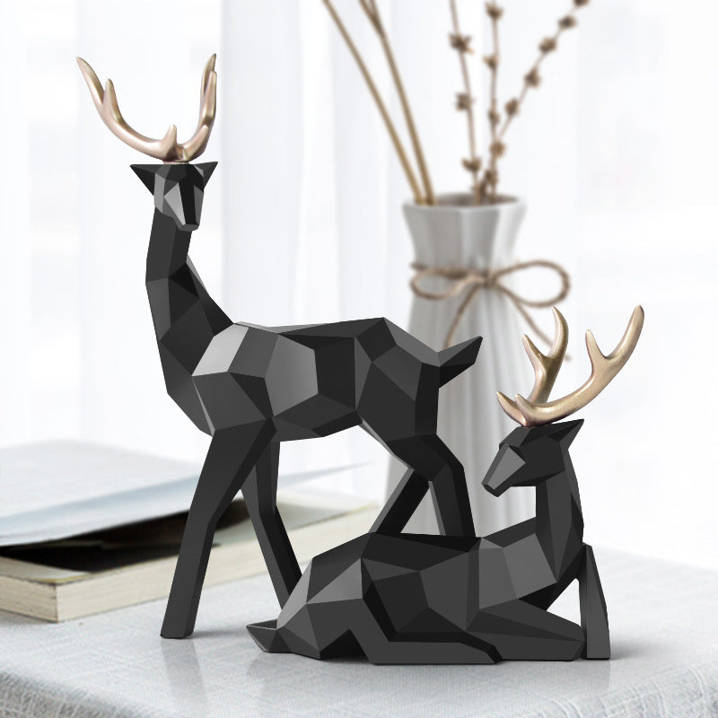 Two black geometric deer figurines on a surface with a vase and branches in the background.