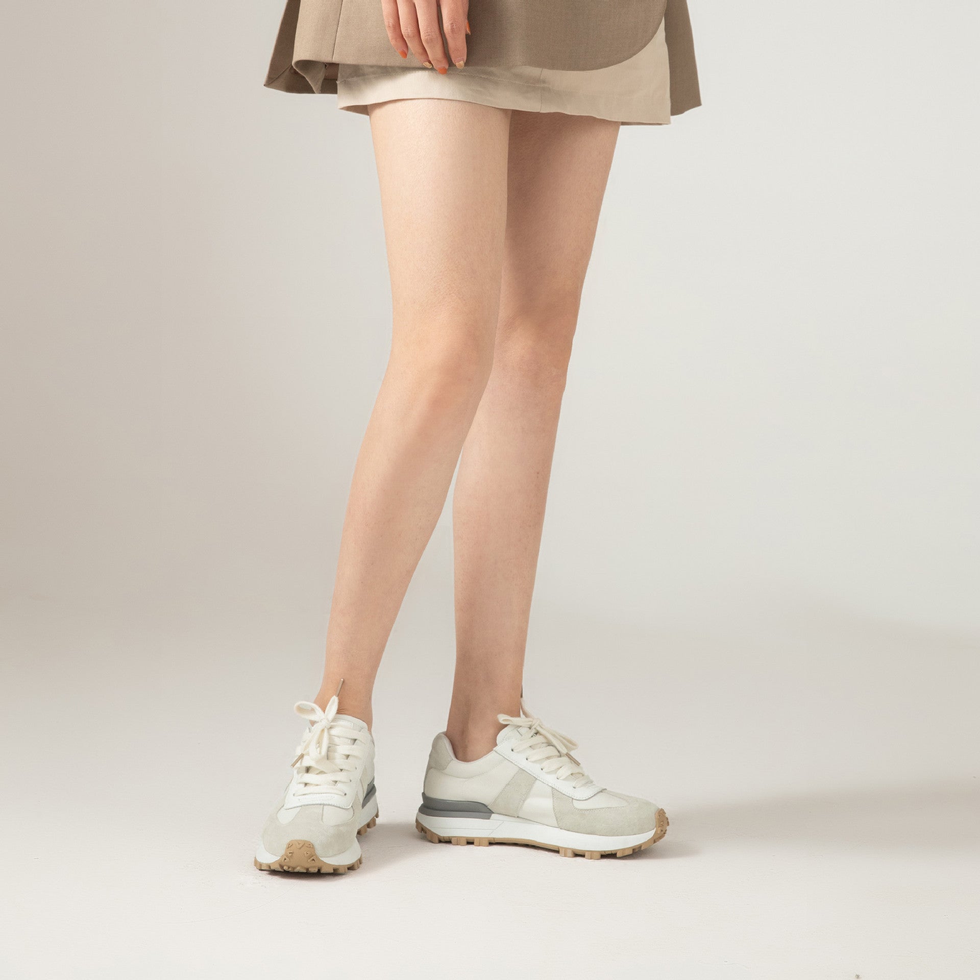 White sneakers worn with a beige skirt on a plain background