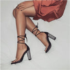 Black strappy high-heeled shoes with glittery details worn by a person in a red satin dress.
