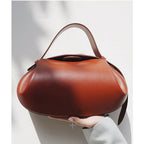 Brown handbag held by a person against a light gray background
