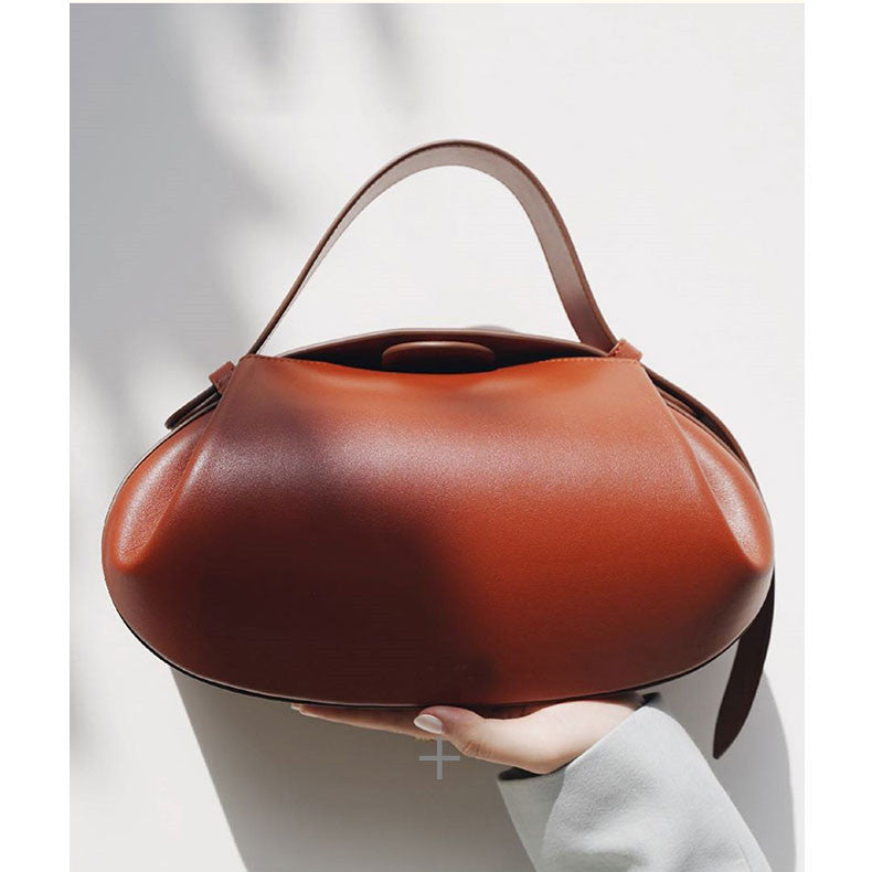 Brown handbag held by a person against a light gray background