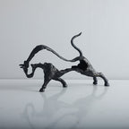Bronze sculpture of a dynamic animal figure on a reflective surface with a neutral background