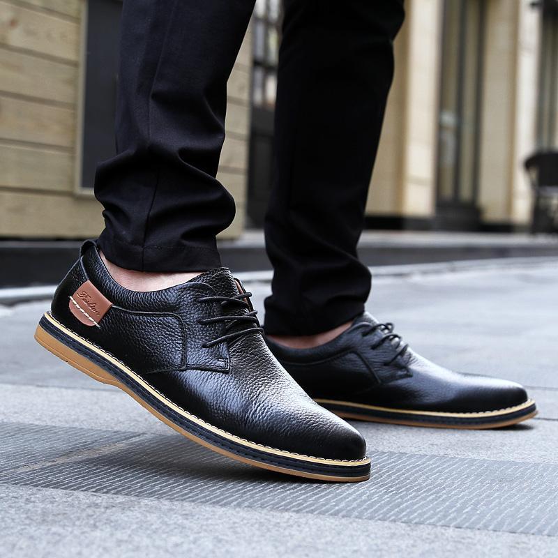 Black leather shoes with brown soles worn by a person on a pavement.
