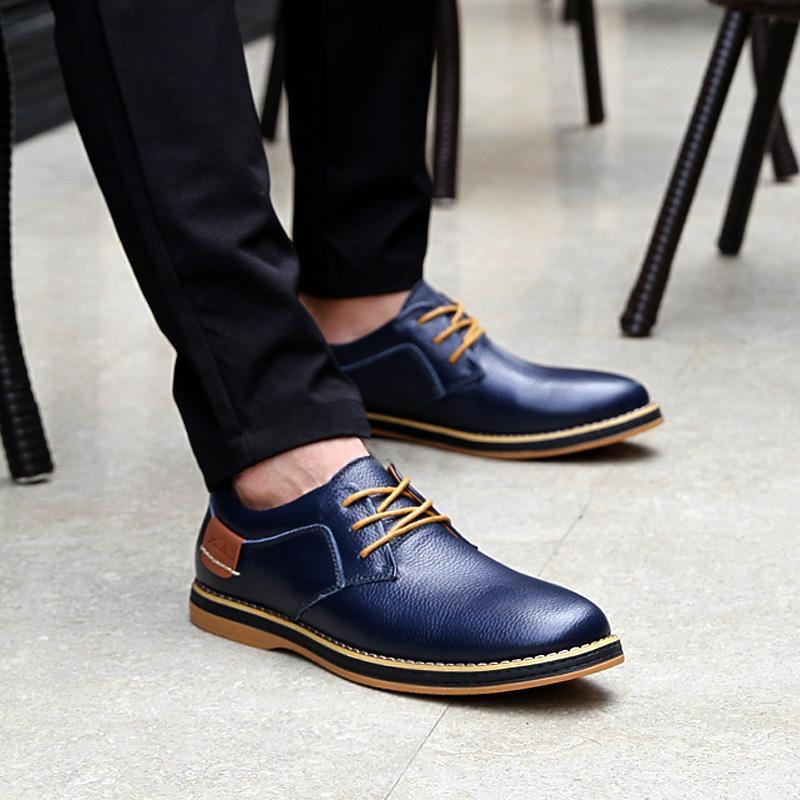 Navy blue leather shoes with brown accents worn by a person on a light gray floor.