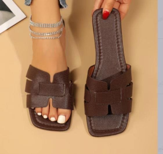 Brown sandal with adjustable straps held by a hand on a beige background