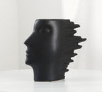 Black ceramic vase shaped like a face with a headdress on a white background