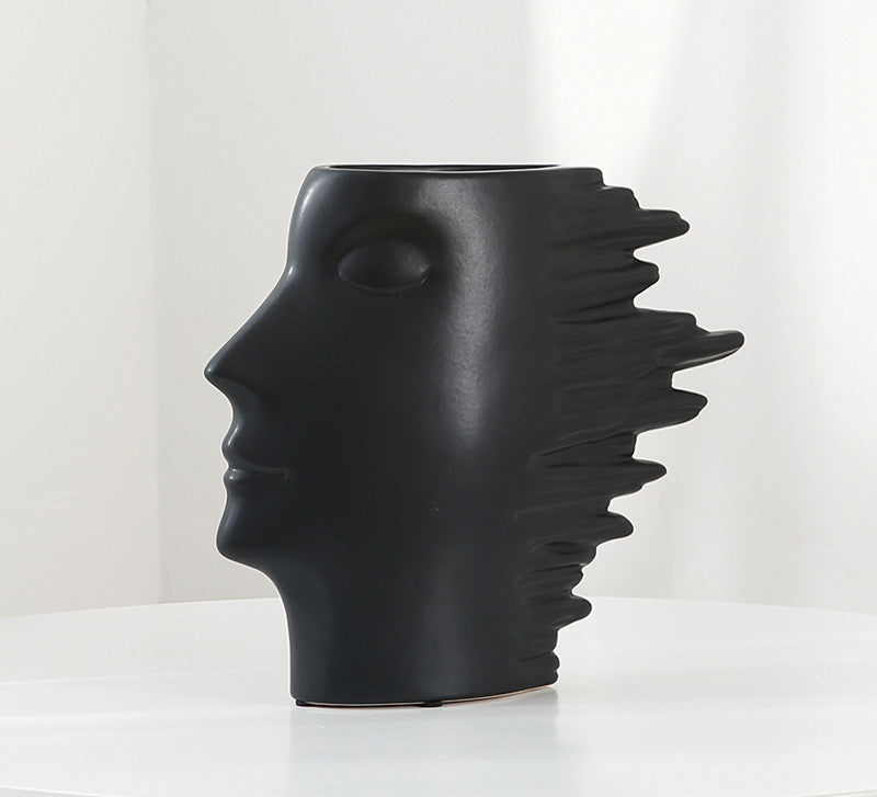 Black ceramic vase shaped like a face with a headdress on a white background