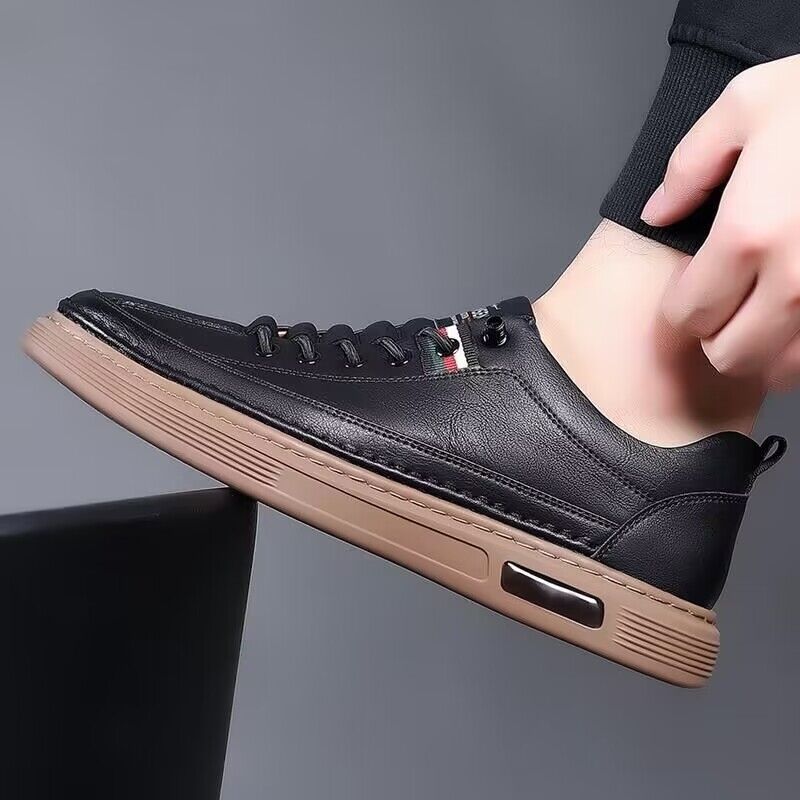 Black leather sneaker with a brown sole worn by a person on a gray background