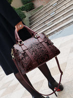 Brown embossed handbag held by a person on a city street.