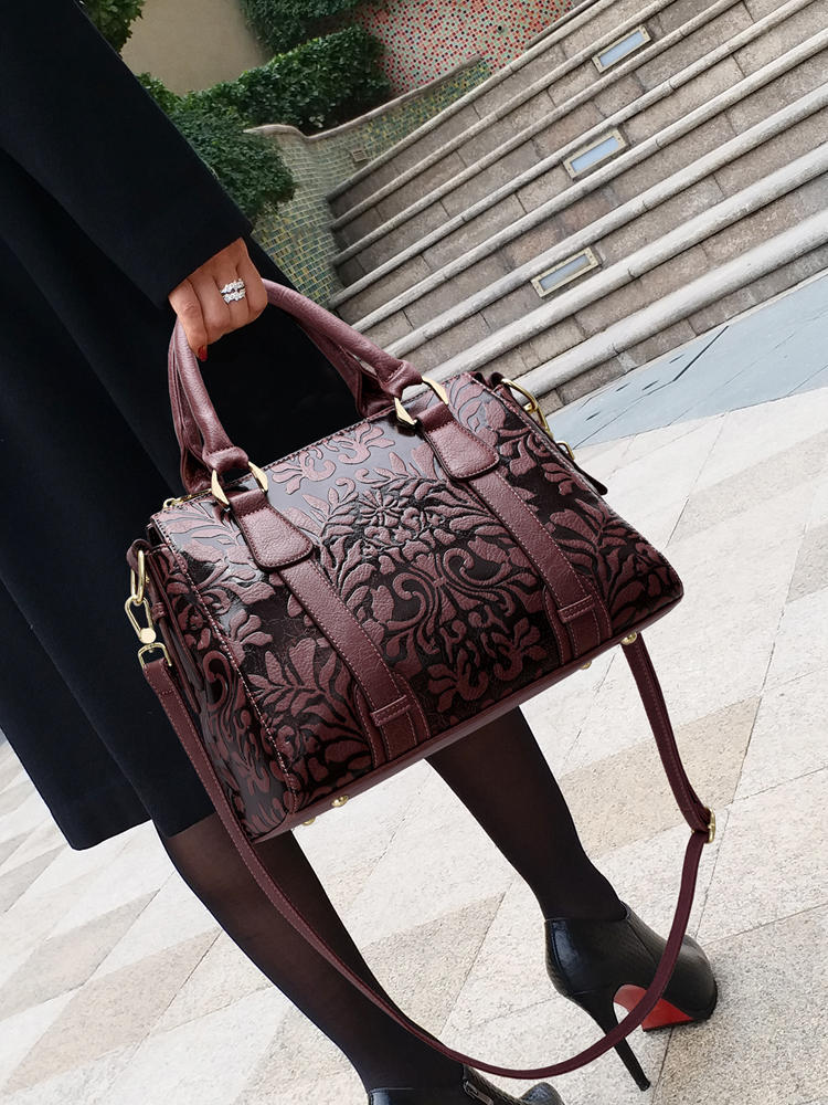 Brown embossed handbag held by a person on a city street.