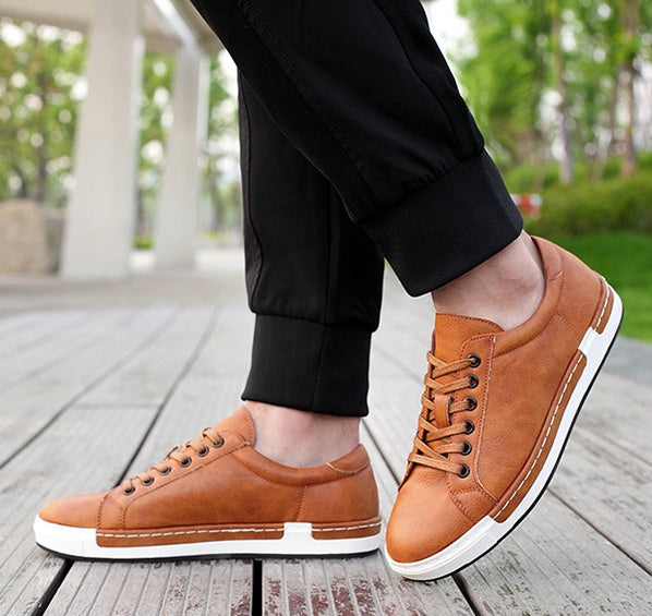 Brown sneakers worn with black pants on a wooden floor.