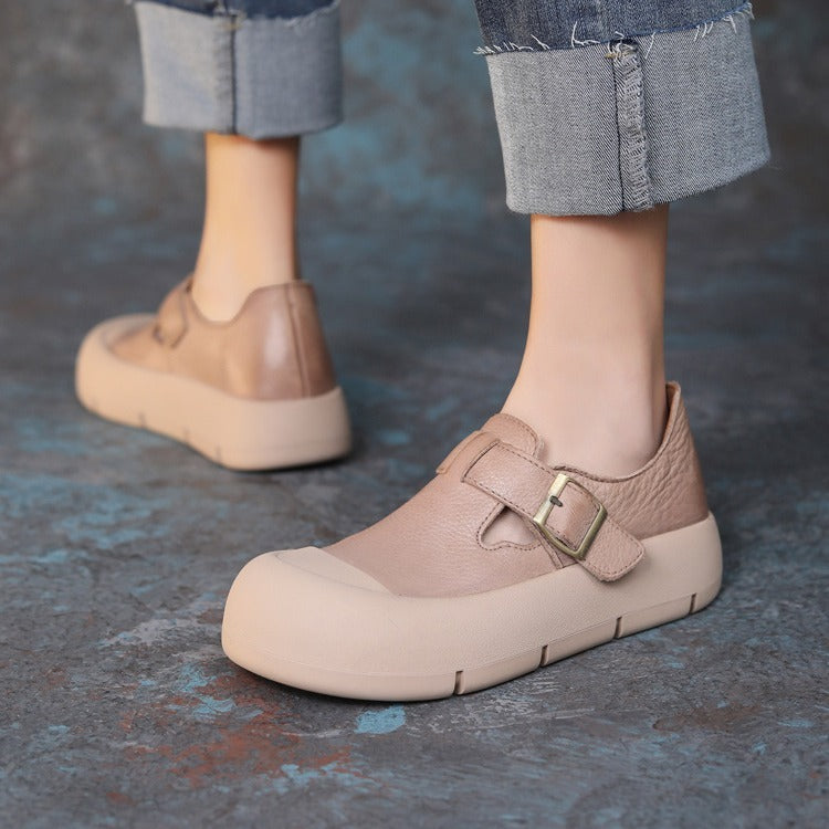 Beige shoes with a strap worn by a person on a textured floor.