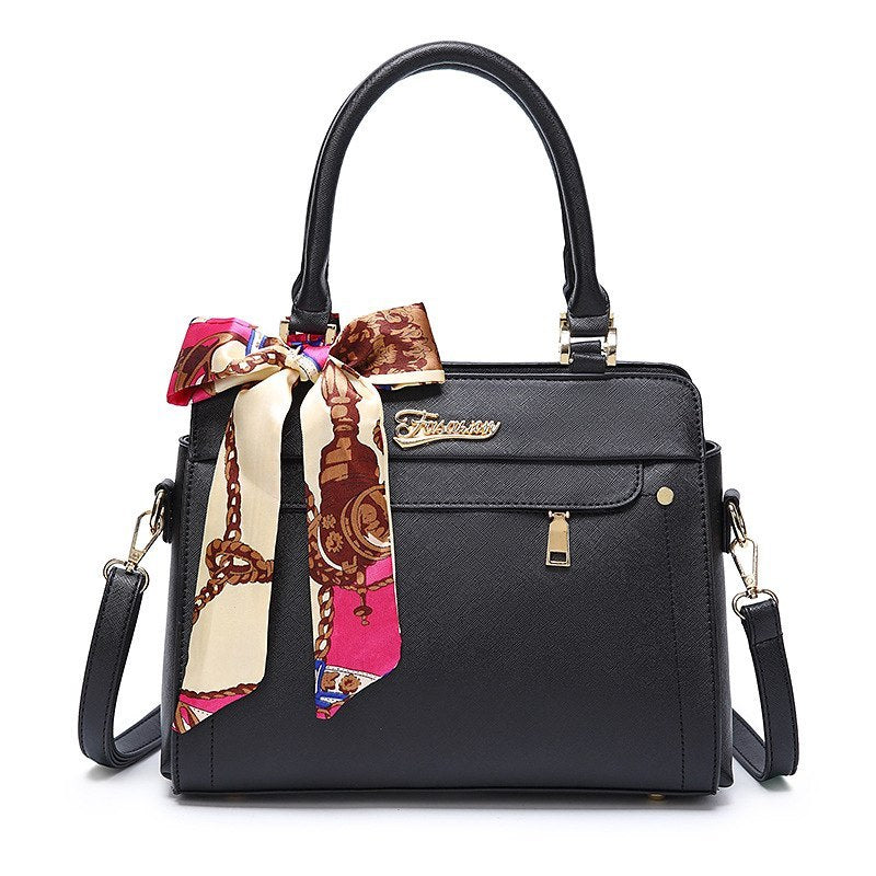 Black handbag with a colorful scarf draped over it on a white background