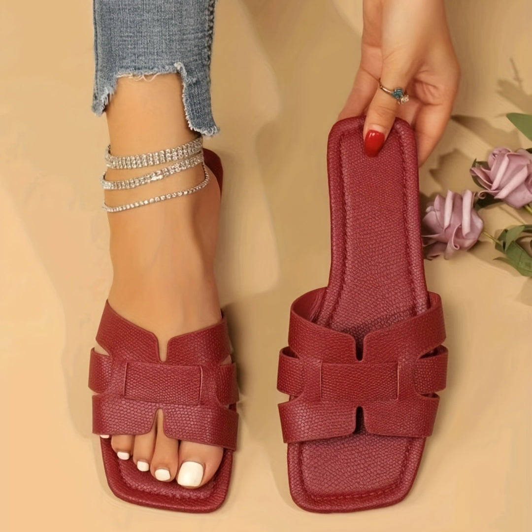 Red sandals being held by a hand on a beige background with flowers.