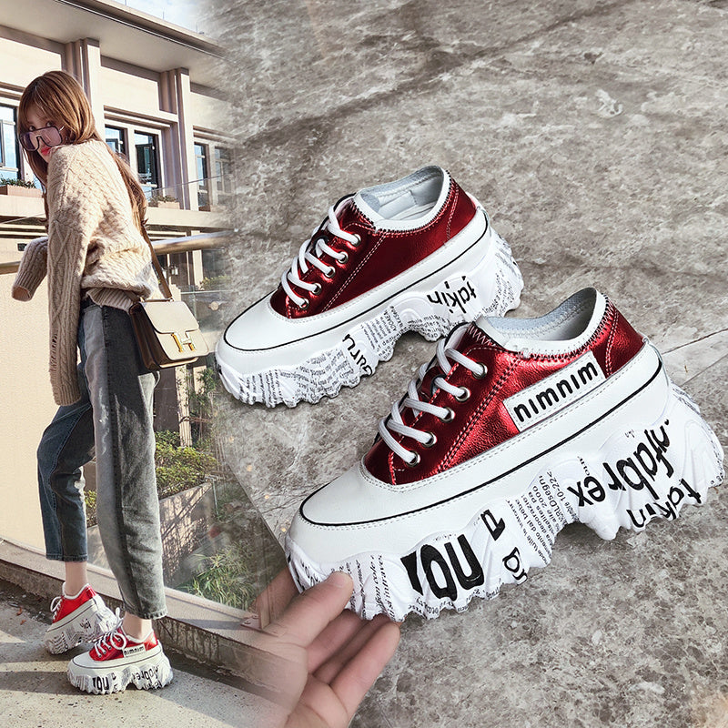 Red sneakers with white soles and text design, worn by a person on a concrete surface.