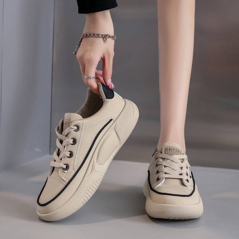 Beige sneakers with black accents held by a hand against a neutral background