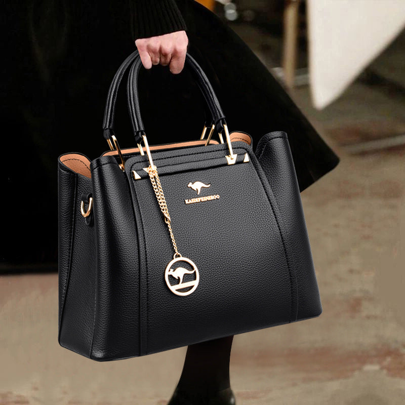 Black handbag with gold chain and logo held by a person wearing a black coat.
