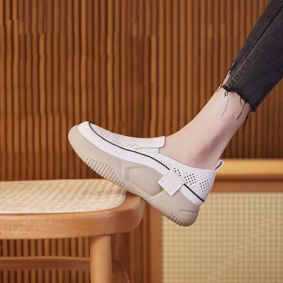 White slip-on shoes with a platform sole worn by a person sitting on a wooden chair.