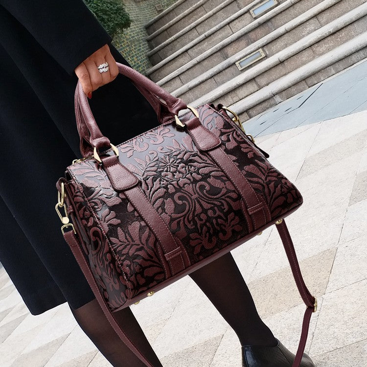 Brown embossed handbag held by a person on a pavement.