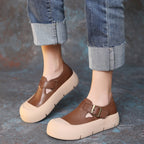 Brown shoes with beige soles worn with rolled-up jeans on a textured surface