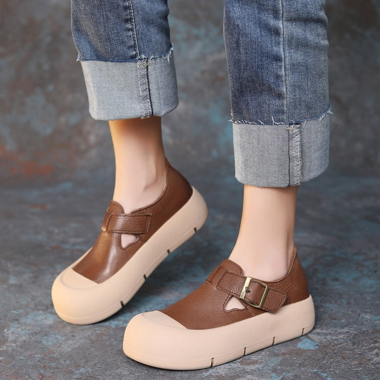 Brown shoes with beige soles worn with rolled-up jeans on a textured surface