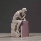 Statue of a thinker next to a pink smartphone on a wooden surface with a dark background