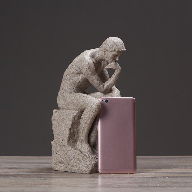 Statue of a thinker next to a pink smartphone on a wooden surface with a dark background