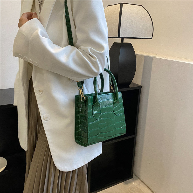 Person holding a green handbag indoors with a lamp in the background