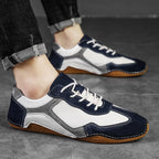 Navy, white, and gray sneakers with brown soles worn by a person on a gray floor.