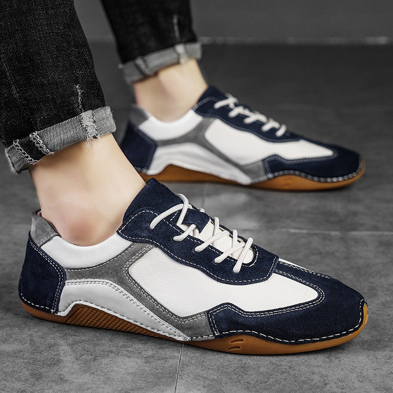 Navy, white, and gray sneakers with brown soles worn by a person on a gray floor.