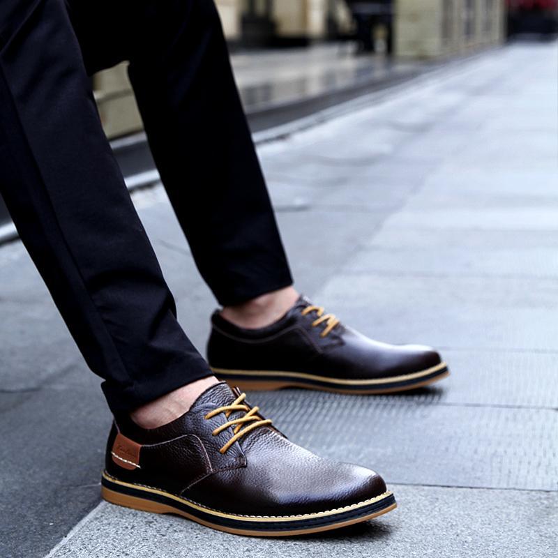 Brown leather shoes worn with black pants on a pavement.