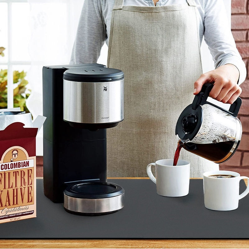 Person pouring coffee from a carafe into a mug next to a coffee maker and a bag of coffee.