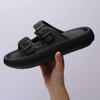 Black sandal with buckle design held by a hand against a light gray background