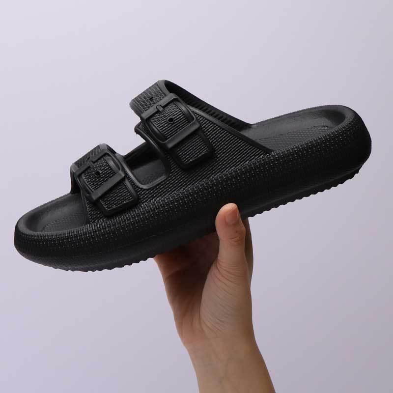 Black sandal with buckle design held by a hand against a light gray background