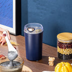 Navy blue salt shaker on a wooden surface with a hand holding a spoon and a jar of mixed beans in the background.