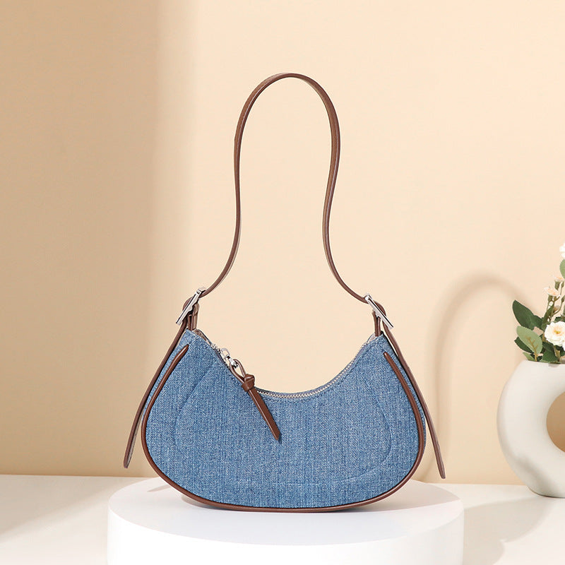Blue denim handbag with brown leather strap on a beige background