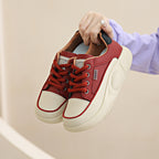 Red sneakers with white soles held by a hand against a neutral background