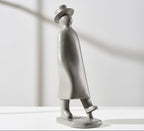 Silver sculpture of a person wearing a hat and coat on a white background
