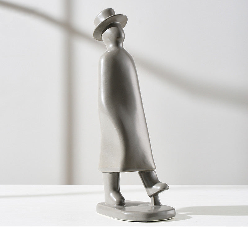 Silver sculpture of a person wearing a hat and coat on a white background