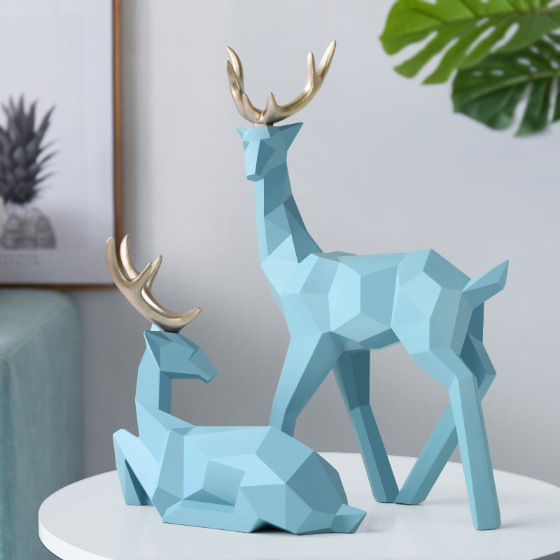 Two blue geometric deer sculptures on a white surface with a neutral background
