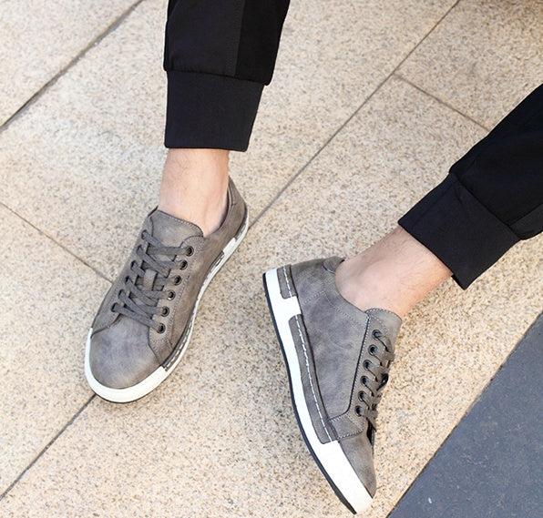Gray sneakers worn on a person's feet on a tiled floor.