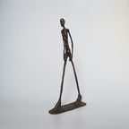 Bronze sculpture of a long-legged figure on a white background